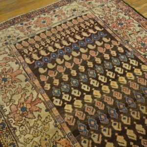 Low-pile rug with a dark field, light floral border, and repeating blue/pink geometric motifs on wood.