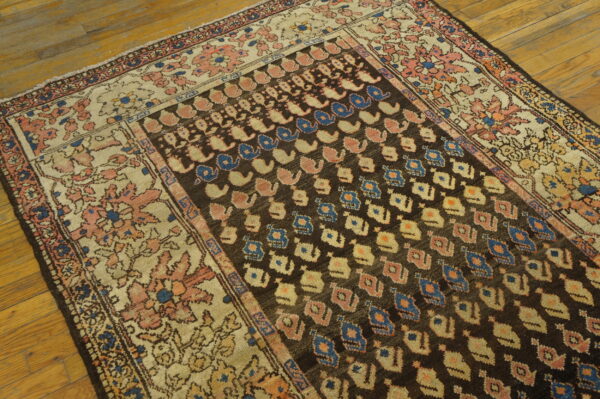 Low-pile rug with a dark field, light floral border, and repeating blue/pink geometric motifs on wood.