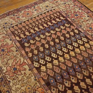 A low-pile rug with a dark brown field, blue/rose motifs, and a wide floral beige border, lying on wood floors.
