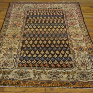 A worn rug featuring a dark brown geometric field and an ivory floral border rests on a glossy wood plank floor.