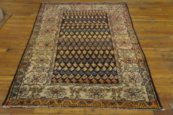 A worn rug featuring a dark brown geometric field and an ivory floral border rests on a glossy wood plank floor.