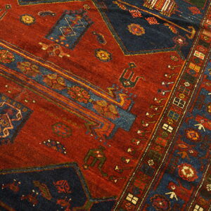Red and dark blue tribal rug showing geometric patterns and multiple borders on light wood floor.