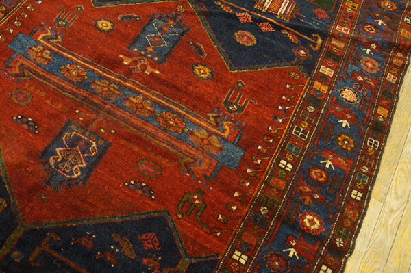 Red and dark blue tribal rug showing geometric patterns and multiple borders on light wood floor.