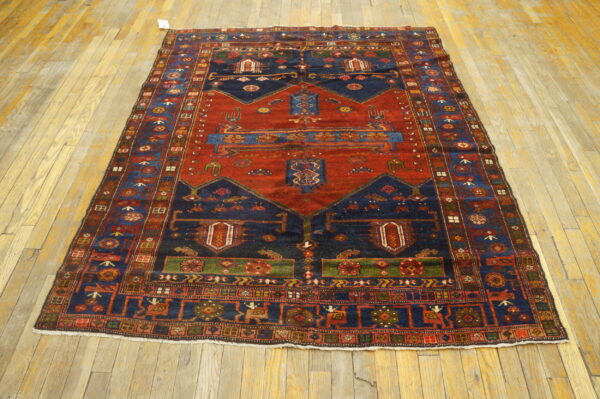 A deep red and navy tribal rug with geometric motifs and multi-layered borders on worn wooden planks.