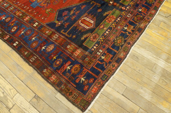 A corner of a red, navy, and green geometric patterned rug rests on rustic light wood floorboards.