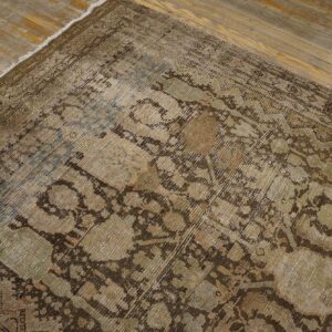 Distressed low-pile rug featuring faded traditional patterns in brown, khaki, and subtle blue on a rustic wooden floor.