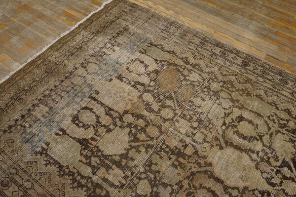 Distressed low-pile rug featuring faded traditional patterns in brown, khaki, and subtle blue on a rustic wooden floor.