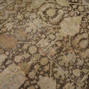 Distressed, low-pile rug close-up showing brown and beige traditional patterns with hints of muted green.