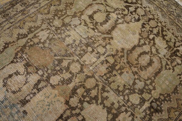 Distressed, low-pile rug close-up showing brown and beige traditional patterns with hints of muted green.