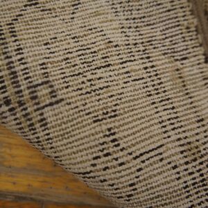 Woven rug backing in beige and dark brown threads curls over distressed yellow-brown hardwood planks.