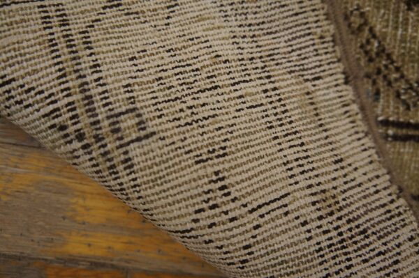 Woven rug backing in beige and dark brown threads curls over distressed yellow-brown hardwood planks.