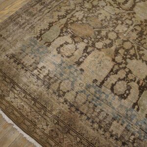 Low-pile, faded rug with traditional brown, green, and blue pattern resting on worn wooden planks.