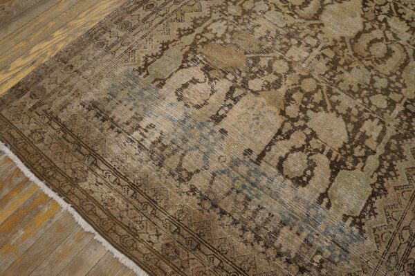 Low-pile, faded rug with traditional brown, green, and blue pattern resting on worn wooden planks.