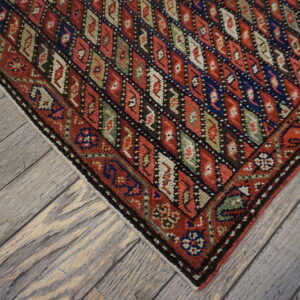 Red and navy geometric diamond pattern rug corner rests on distressed gray hardwood flooring.