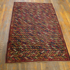 Red and navy geometric rug with repeating olive and cream diamonds resting on wood plank flooring.