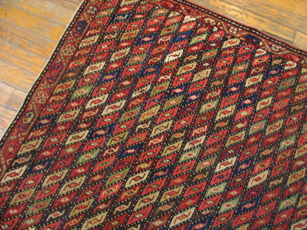 Geometric rug featuring repeating red, blue, green, and tan diamonds rests on polished wood flooring.