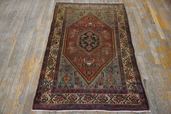 Multi-colored low-pile rug featuring a rust and sage geometric pattern rests on distressed gray wood flooring.
