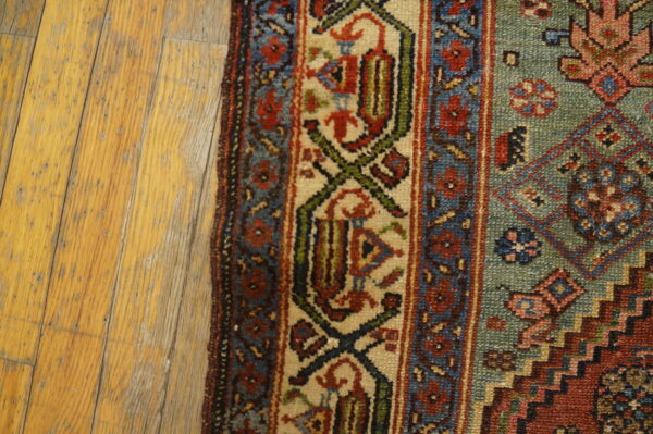 Close-up of a traditionally patterned rug with red, blue, green, and beige accents beside light wood flooring.