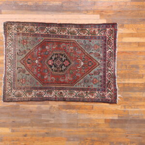 Red, sage, and black geometric patterned area rug lying on distressed light brown wood planks.