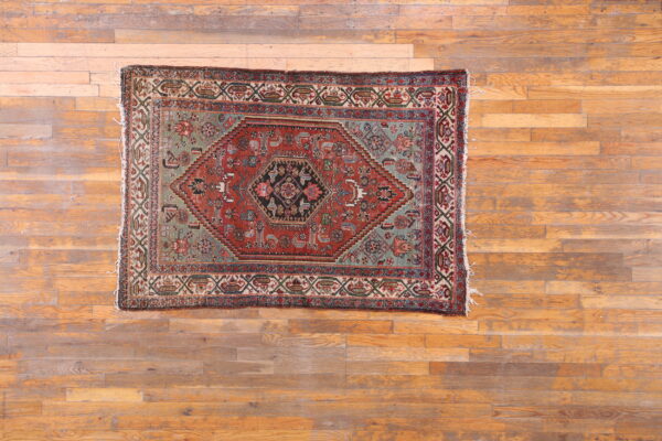 Red, sage, and black geometric patterned area rug lying on distressed light brown wood planks.