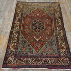 Low-pile geometric rug in rust, teal, navy, and cream on gray and yellow distressed wood flooring.