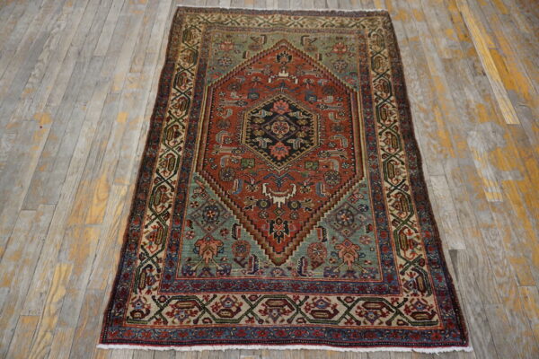 Low-pile geometric rug in rust, teal, navy, and cream on gray and yellow distressed wood flooring.