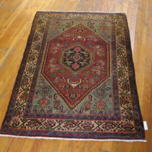 Geometric red rug with blue and teal highlights features a central medallion on light wood flooring.