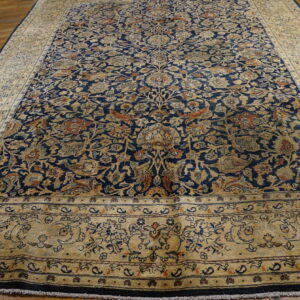 Indigo floral rug with dense tan and rust patterns, laid out on a glossy wood floor.