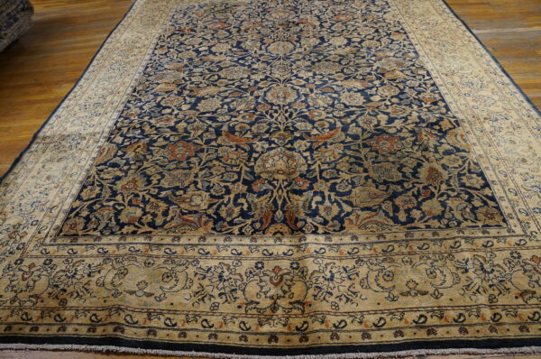 Indigo floral rug with dense tan and rust patterns, laid out on a glossy wood floor.