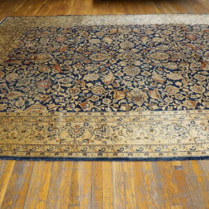 Low pile rug with navy blue and gold intricate floral patterns rests on a visible plank hardwood floor.