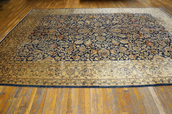 Low pile rug with navy blue and gold intricate floral patterns rests on a visible plank hardwood floor.