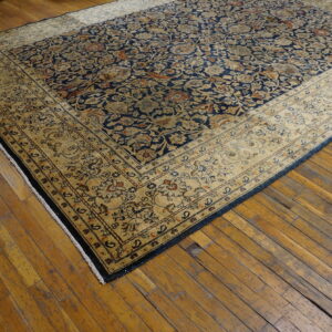 Intricate navy blue and tan rug featuring a wide border covers a worn hardwood floor.
