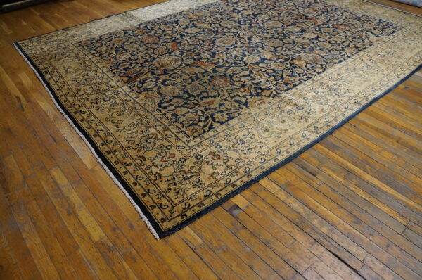 Intricate navy blue and tan rug featuring a wide border covers a worn hardwood floor.