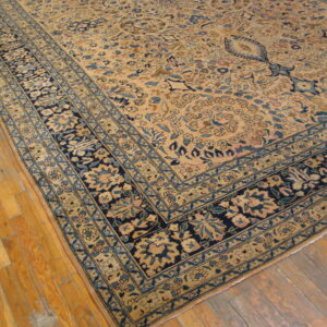 Beige floral rug with navy and light blue borders lies on honey-toned wood flooring.
