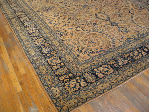 Beige floral rug with navy and light blue borders lies on honey-toned wood flooring.