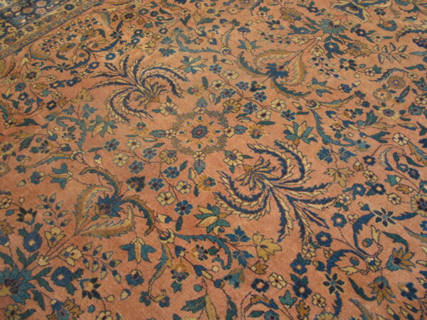 Low-pile rug with a coral field and a dense all-over pattern of blue, teal, and gold florals.