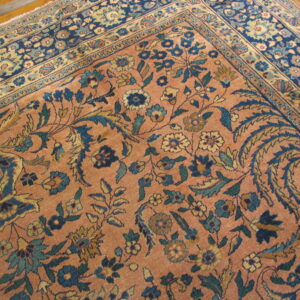 Detailed view of a low-pile traditional rug featuring salmon, blue, and yellow floral patterns on a hardwood floor.
