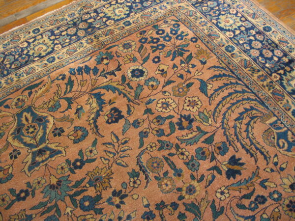 Detailed view of a low-pile traditional rug featuring salmon, blue, and yellow floral patterns on a hardwood floor.