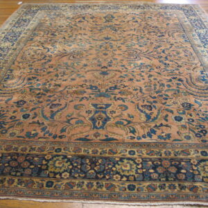 Peach and blue traditional rug with a dense floral pattern lying on polished wood floors.