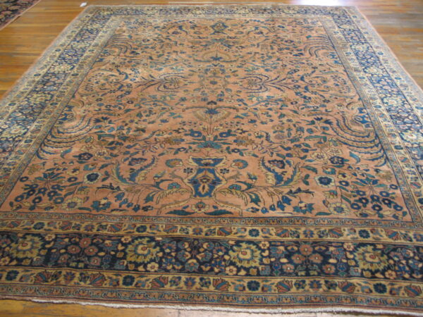 Peach and blue traditional rug with a dense floral pattern lying on polished wood floors.