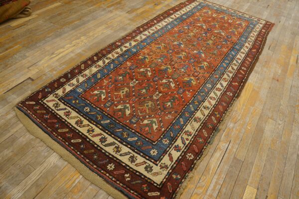 A rust red rug with tribal geometric patterns and a blue and cream border lies on light wood planks.