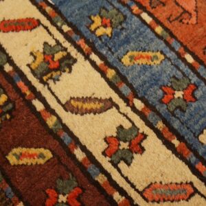 High-pile rug surface showing bands of blue, cream, and rust with geometric and floral patterns over wood flooring.