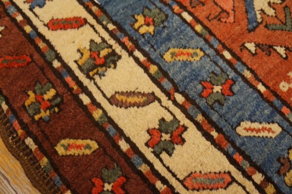 High-pile rug surface showing bands of blue, cream, and rust with geometric and floral patterns over wood flooring.
