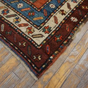 Detail of a traditional red, blue, and cream patterned rug resting on weathered gray wood planks.