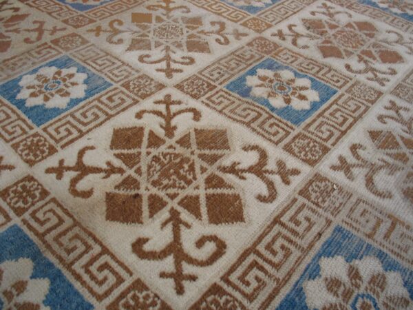 Off-white rug with a geometric grid pattern in rust brown and bright blue floral squares.