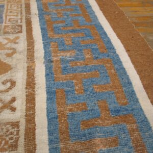 Blue, tan, and cream rug featuring geometric and scrollwork patterns on light brown wooden floors.