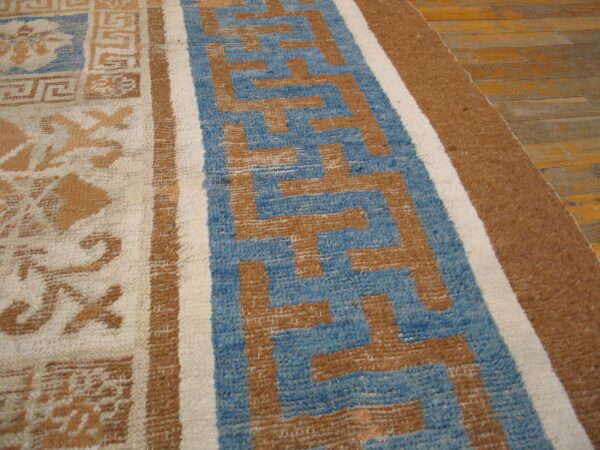 Blue, tan, and cream rug featuring geometric and scrollwork patterns on light brown wooden floors.