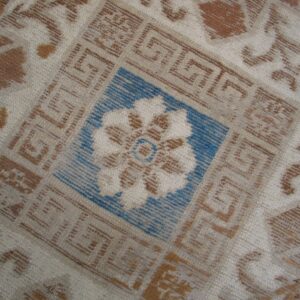Cream, brown, and blue rug detail featuring geometric Greek key borders around a central floral motif.