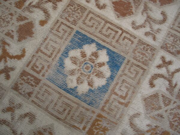 Cream, brown, and blue rug detail featuring geometric greek key borders around a central floral motif.