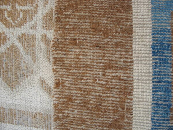 Textured rug detail displaying a cream and brown pattern next to vertical stripes of brown, cream, and blue.